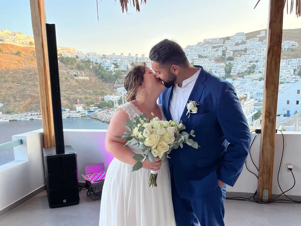 Bernhard and Lisa kissing on a rooftop terrace above a white village.